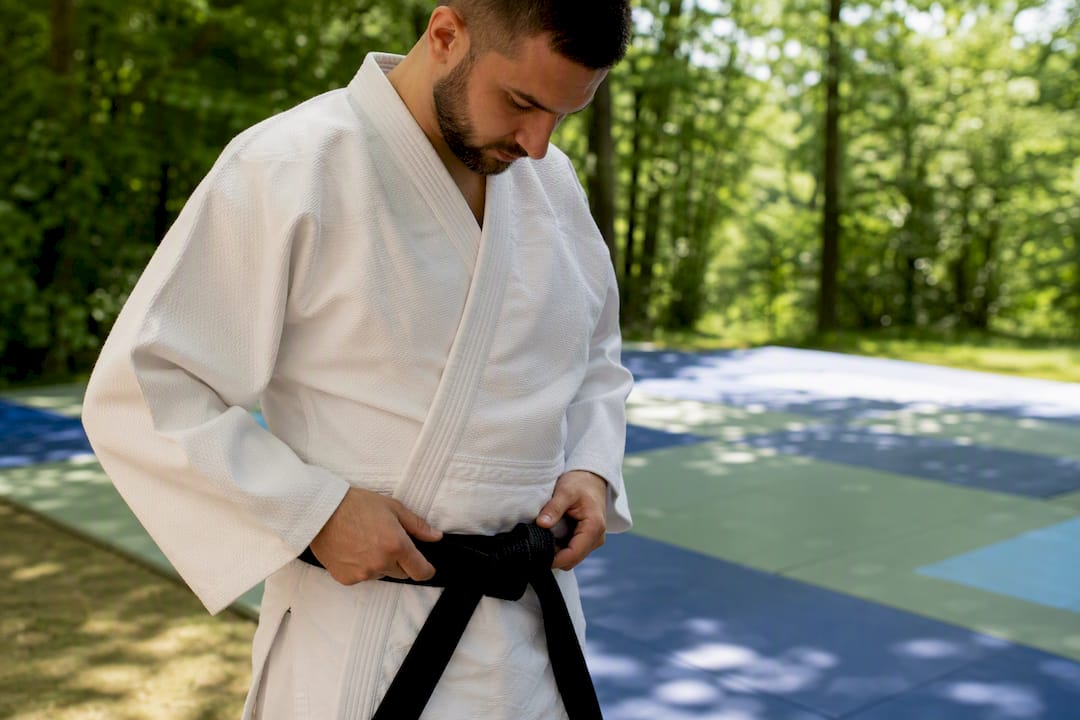 Student tying martial arts belt in dojo